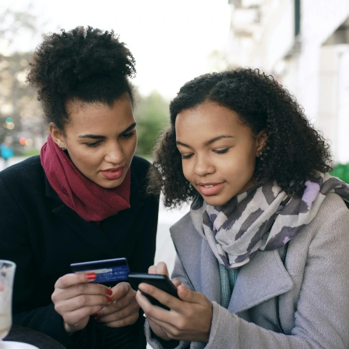 Two women looking at a smartphone with credit card