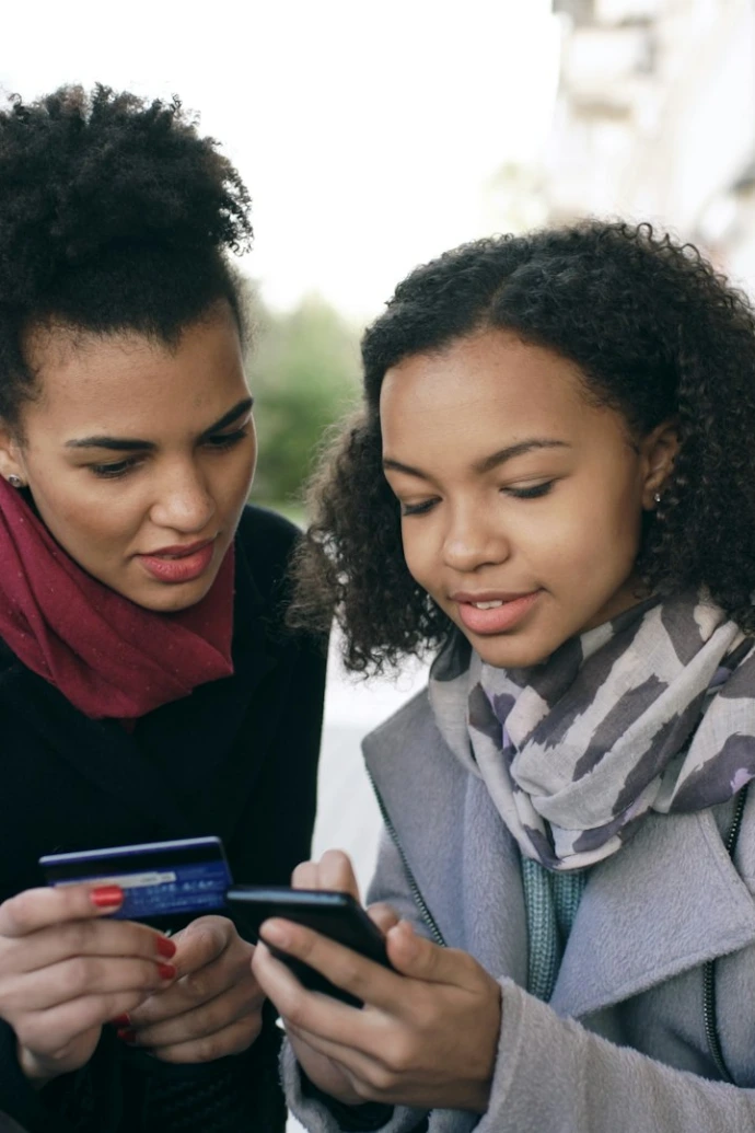 Two women looking at a smartphone with credit card